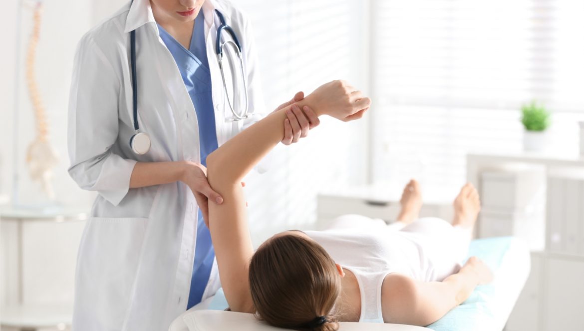 Łokieć tenisisty - jak rozpoznać i jak leczyć? Pani doktor ortopeda bada łokieć pacjentki, leżącej na łóżku lekarskim w gabinecie.