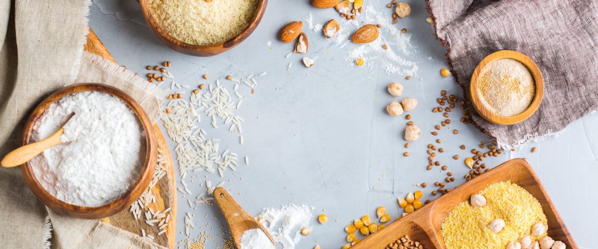 Mąki bezglutenowe: kokosowa, kukurydziana, migdałowa, z ciecierzycy, ryżowa. Mąki bez glutenu w miseczkach na błękitnym blacie.