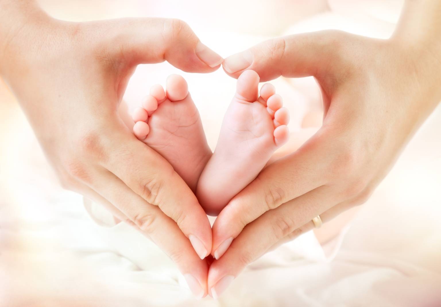 Leczenie niepłodności. Zbliżenie na dłonie kobiety, która trzyma w nich stopy niemowlęcia, uformowane w kształt serca.