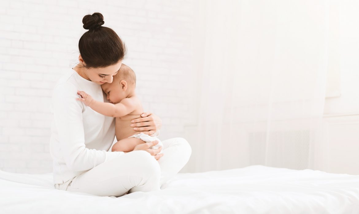 Rozstęp mięśni prostych brzucha po porodzie. Mama w bieli przytula niemowlaka.
