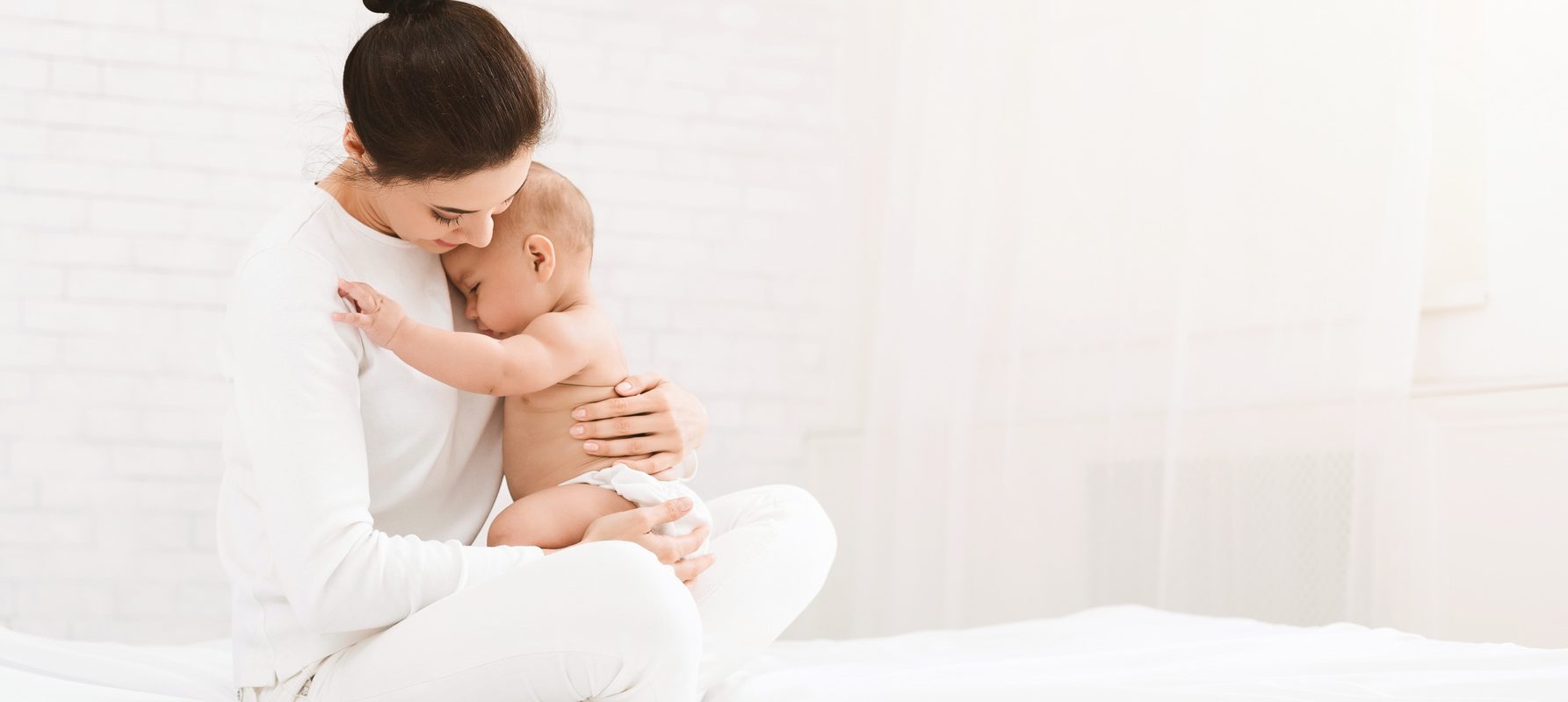 Rozstęp mięśni prostych brzucha po porodzie. Mama w bieli przytula niemowlaka.