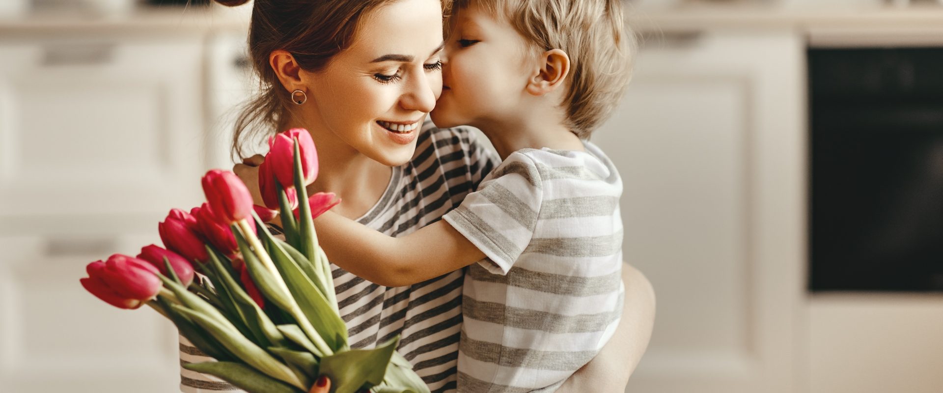 Naturalnie o miłości pisze Beata Sadowska. Synek przytula mamę i wręcza jej bukiet tulipanów w domowej kuchni.