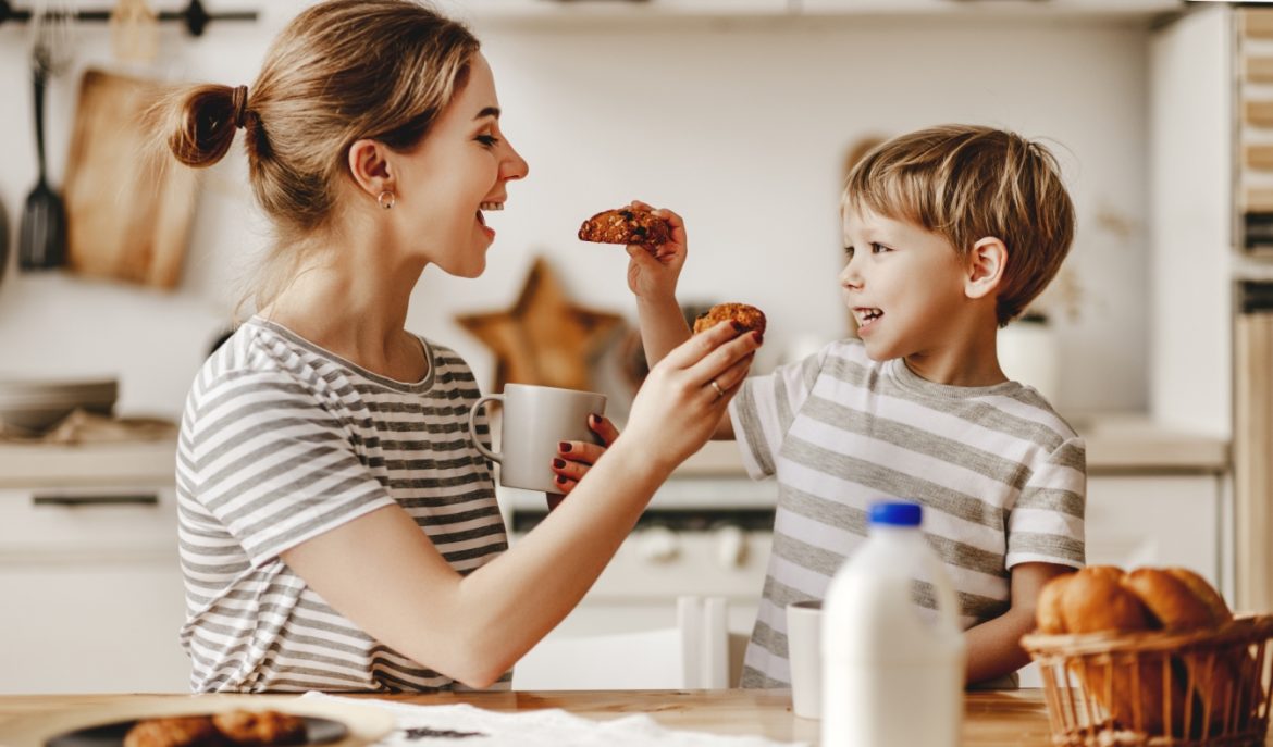 Dlaczego wspólne posiłki są ważne dla dzieci? Mama i synek częstują się nawzajem ciasteczkami, siedząc przy stole w kuchni.