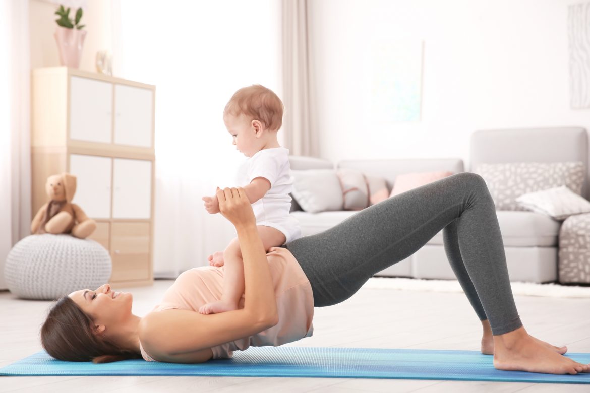 Ćwiczenia po porodzie - jak je wykonać i jakie będą bezpieczne? Mama ćwiczy z niemowlakiem na biodrach na macie w domu.