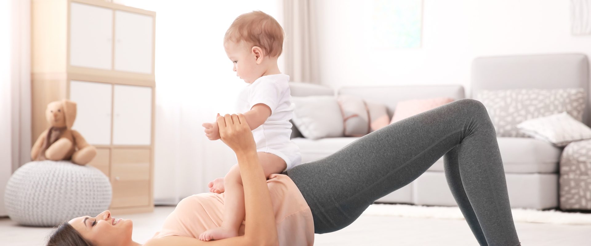 Ćwiczenia po porodzie - jak je wykonać i jakie będą bezpieczne? Mama ćwiczy z niemowlakiem na biodrach na macie w domu.