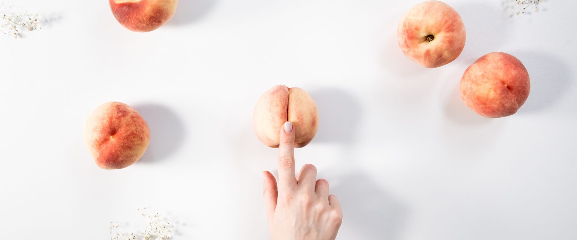 Masturbacja kobiet - jak się masturbować. Kobieca dłoń naciska palcem na wgłębienie w brzoskwini. Obok na blacie leżą inne brzoskwinie.