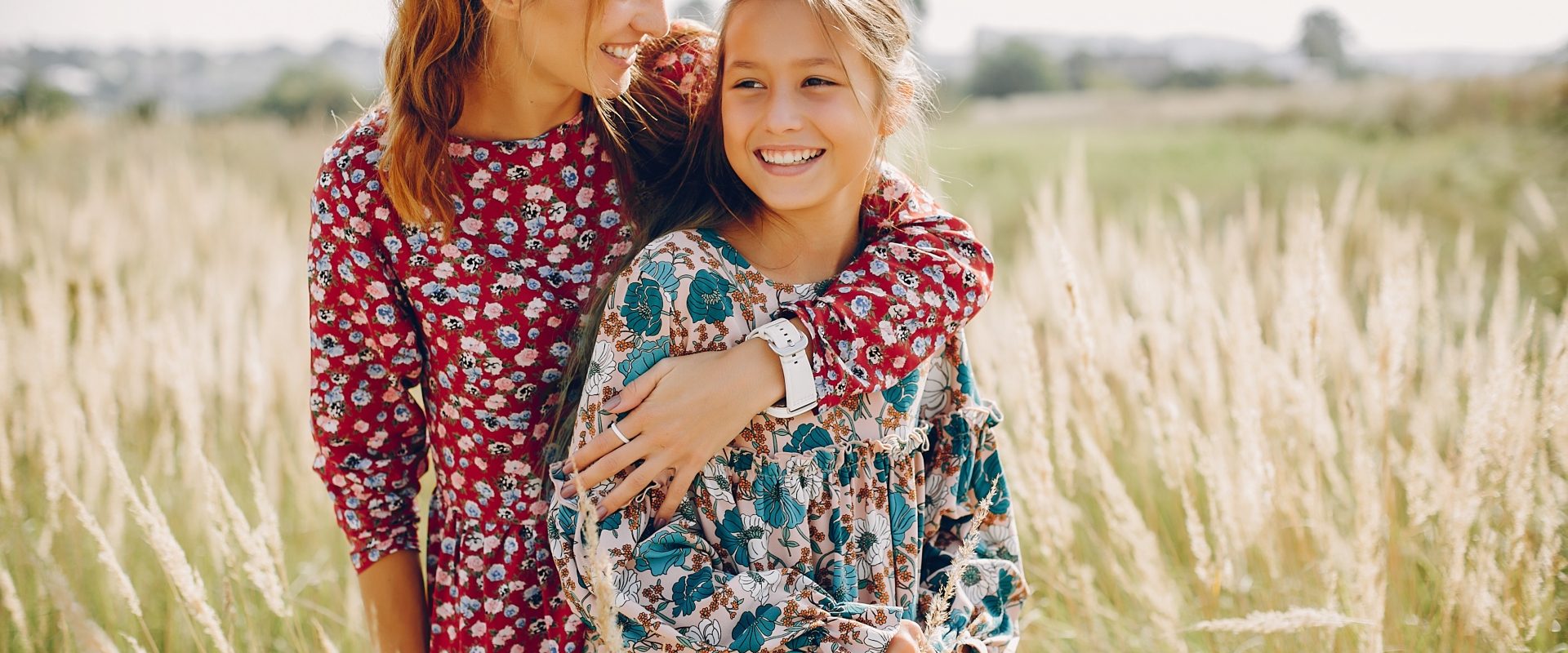 Alergia na pyłki - co musisz o niej wiedzieć? Przytulone mama i córka ubrane w kwieciste sukienki stoją w polu zbóż.