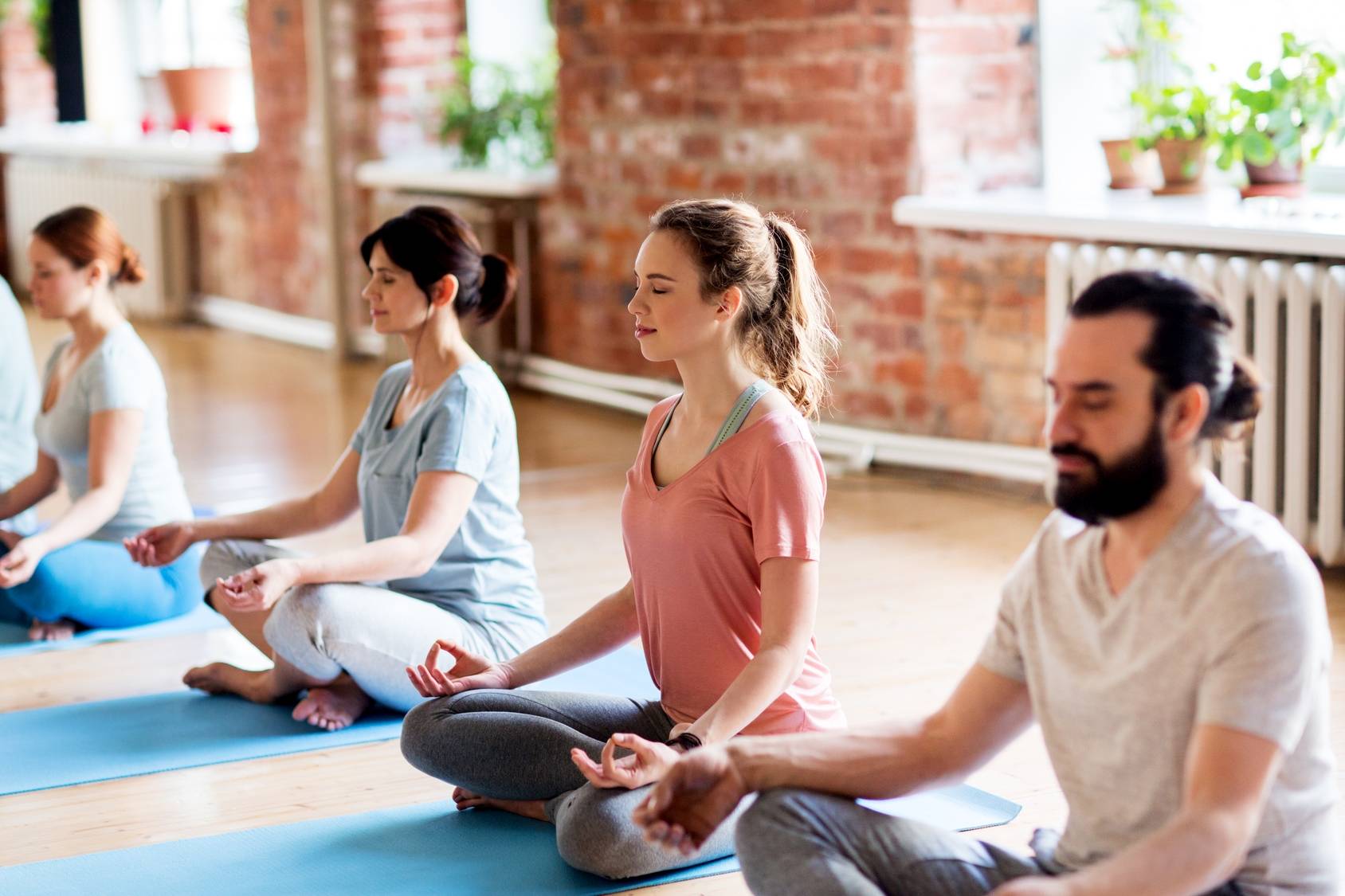 Uczestnicy zajęć jogi medytują na sali gimnastycznej. Jak radzić sobie z napięciem przedmiesiączkowym?