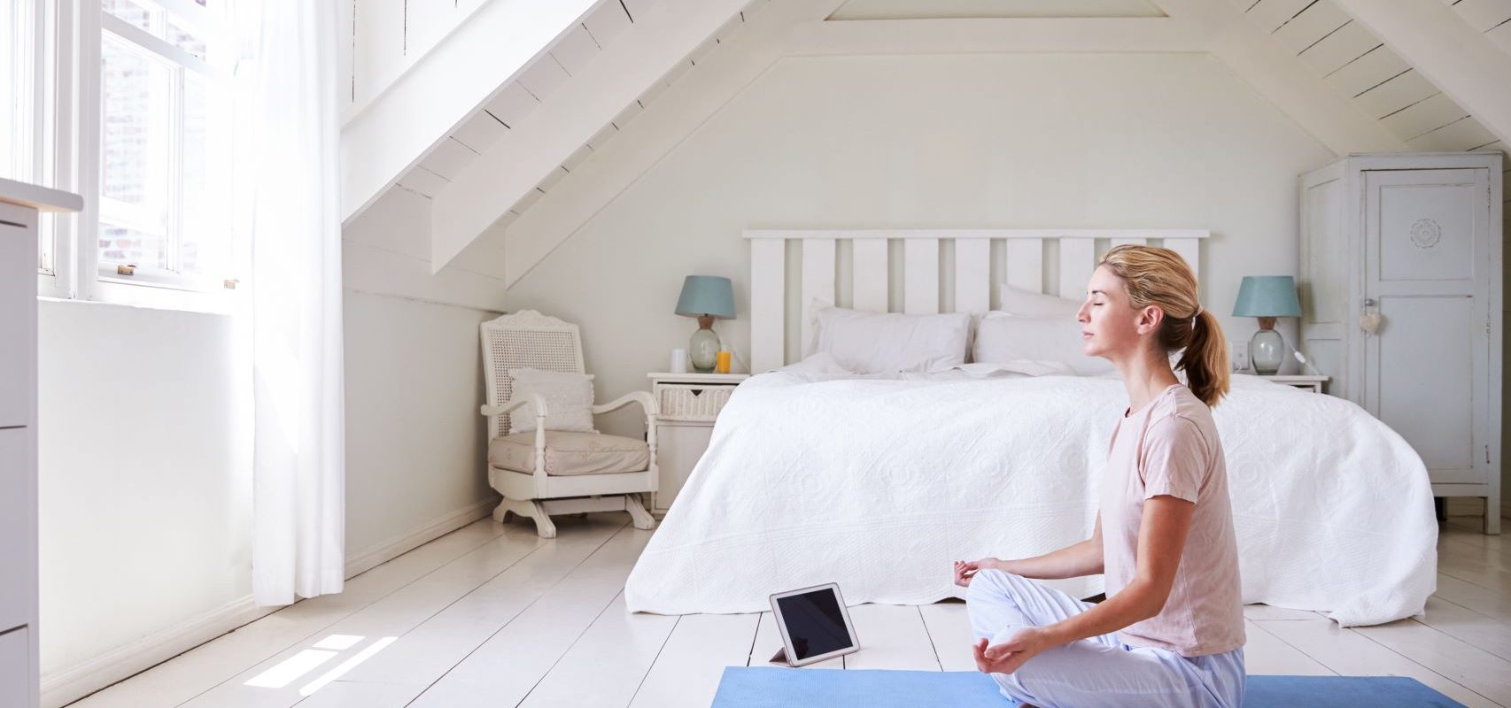 Jak działa aplikacja do medytacji? Kobieta medytuje w swojej sypialni korzystając z aplikacji na tablecie.