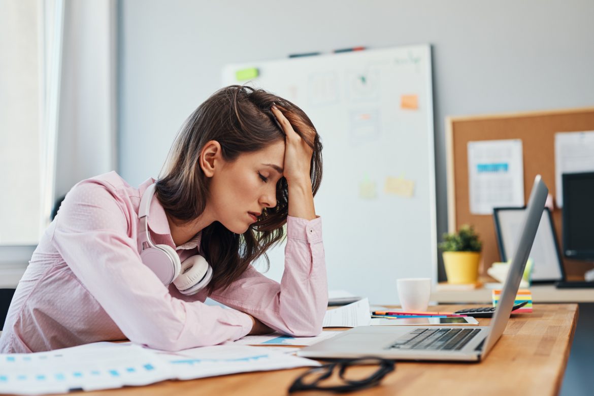 Magnez pomaga zmniejszyć ból migrenowy. Migrena - czy można jej zapobiec? Kobieta z bólem głowy siedzi przy laptopie.