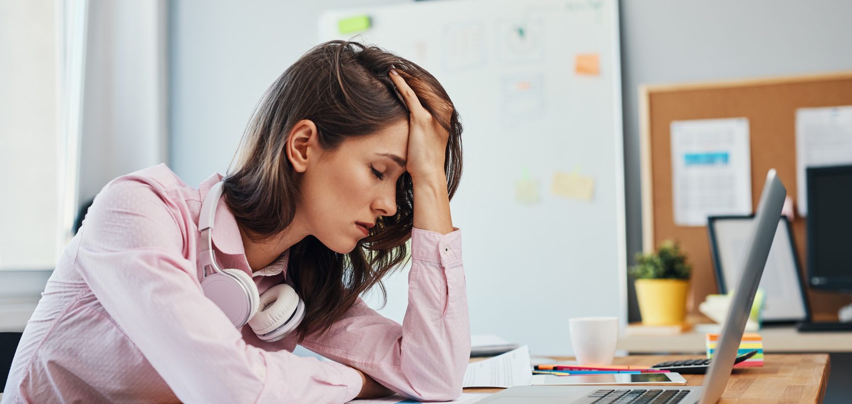 Magnez pomaga zmniejszyć ból migrenowy. Migrena - czy można jej zapobiec? Kobieta z bólem głowy siedzi przy laptopie.