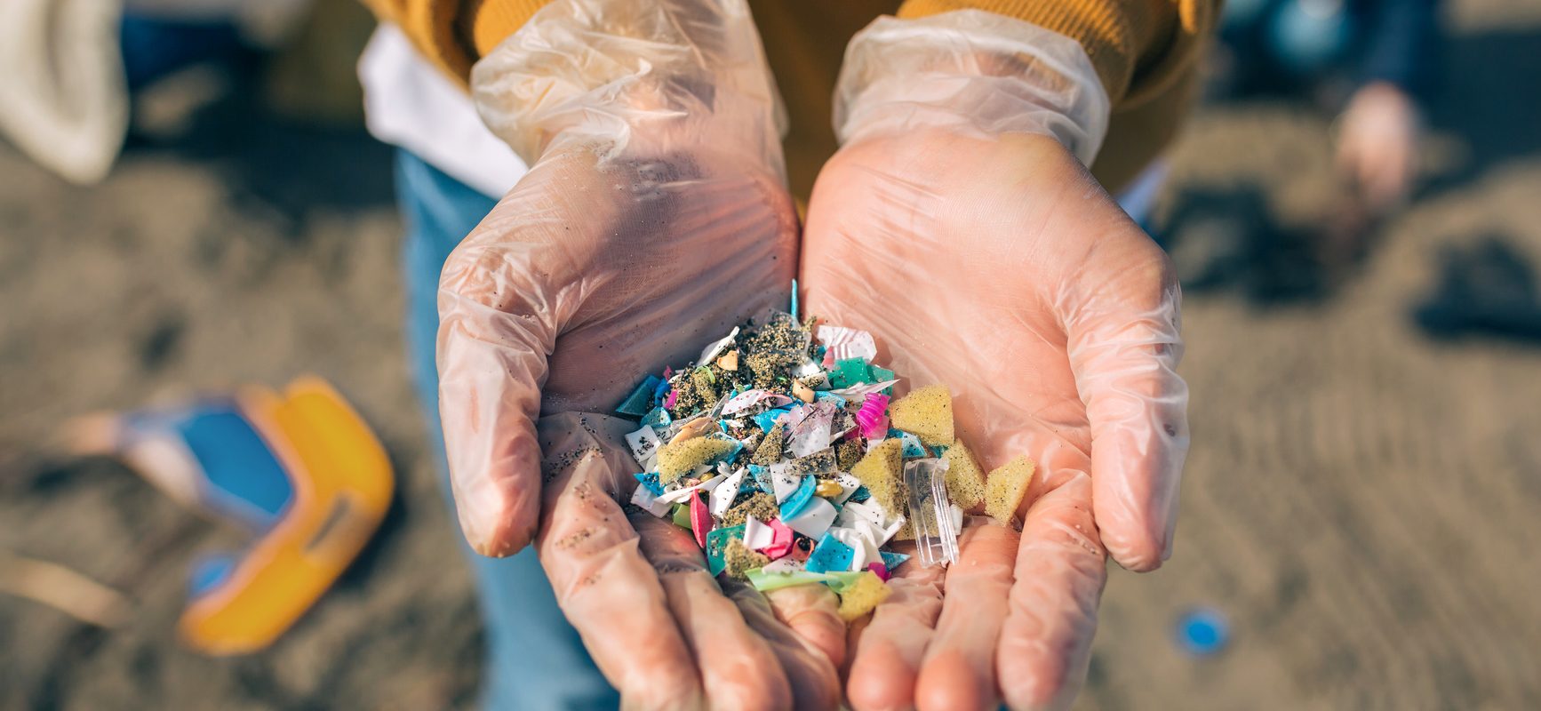 Mikroplastik - jak bardzo jest szkodliwy? Kobieta pokazuje na dłoniach małe cząsteczki plastiku zebrane na plaży.