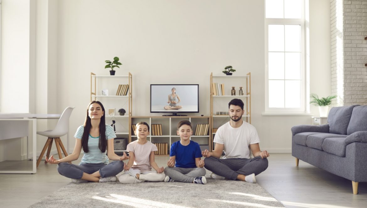 Mindfulness dla dzieci. Rodzina - mama, tata i dwójka dzieci - trenują uważność i medytują w salonie w domu.