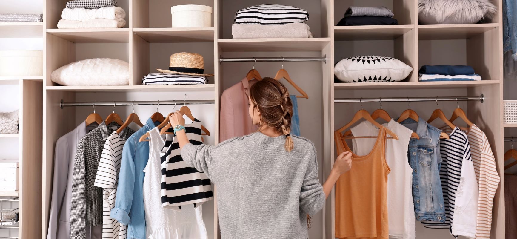 Minimalizm w szafie - jak go osiągnąć? Kobieta stoi przed swoją szafą, w której ma poukładane ubrania.