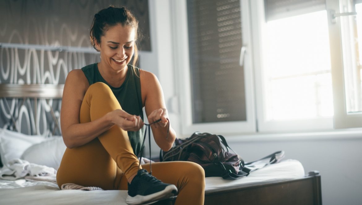Ile ruchu dziennie wystarczy, aby być zdrową? Kobieta siedzi na łóżku w sypialni i zakłada adidasy przed treningiem lub spacerem.