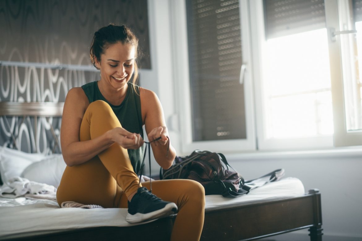 Ile ruchu dziennie wystarczy, aby być zdrową? Kobieta siedzi na łóżku w sypialni i zakłada adidasy przed treningiem lub spacerem.