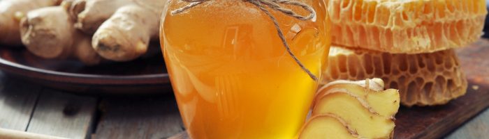 Miód imbirowy (syrop imbirowy) na przeziębienie - sprawdź przepis. Słoik miodu stoi na drewnianej desce, w tle leżą plastry miodu i korzenie imbiru.