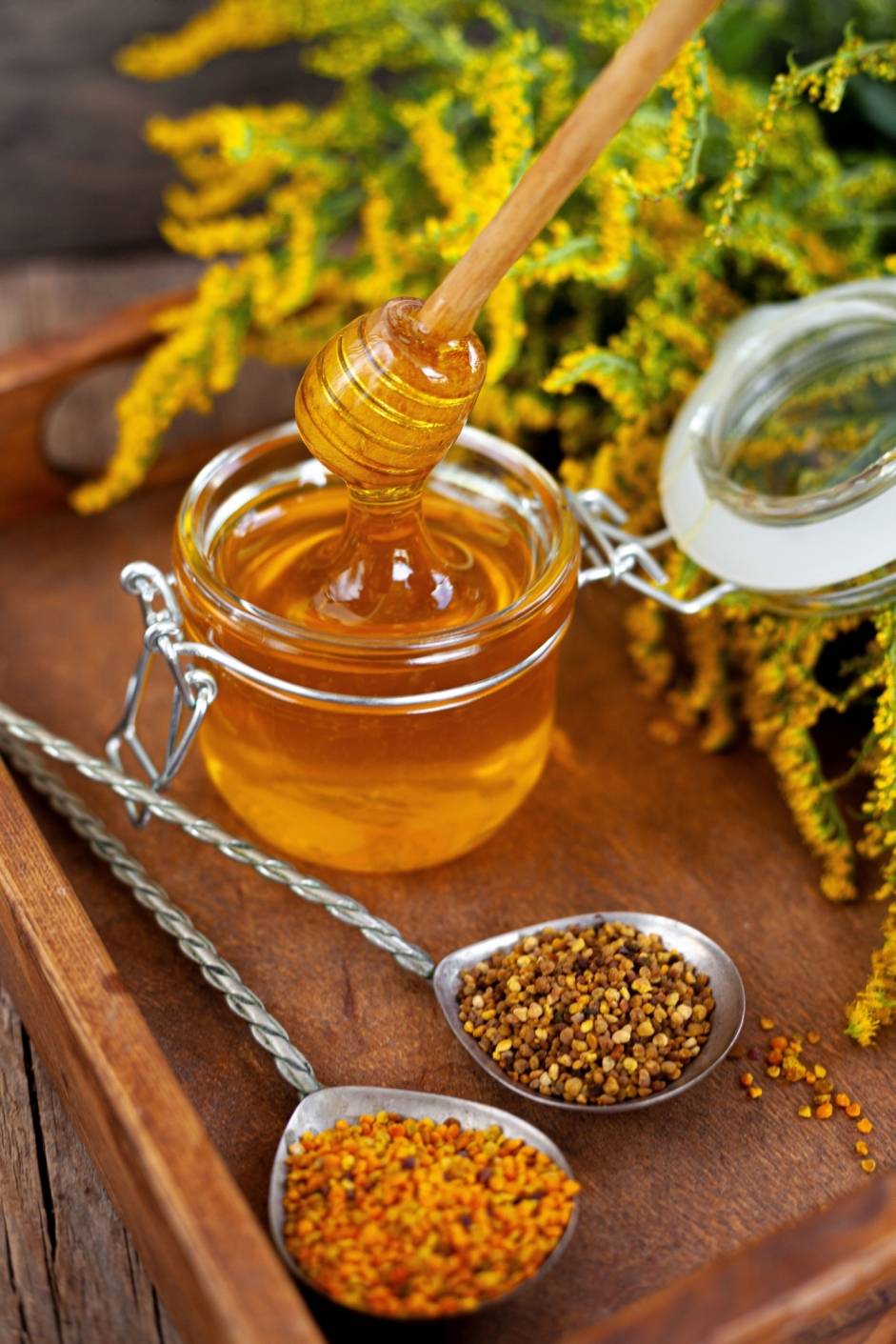 Jak stosować propolis? Płynny miód w słoiku i propolis na stalowych łyżkach na drewnianej tacy.