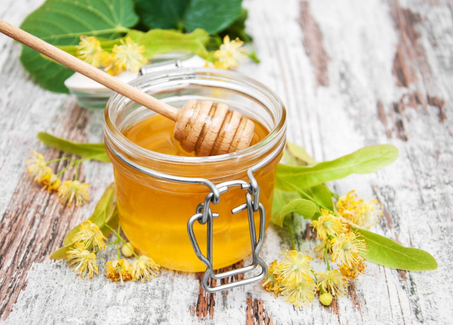 Lipa z miodem. Miód w słoiku na rustykalnym blacie, obok leży gałązka z kwiatami lipy.
