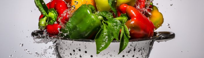 Jak myć owoce i warzywa? Na czym polega ekologiczne mycie warzyw i owoców? Papryki w durszlaku opryskane wodą.