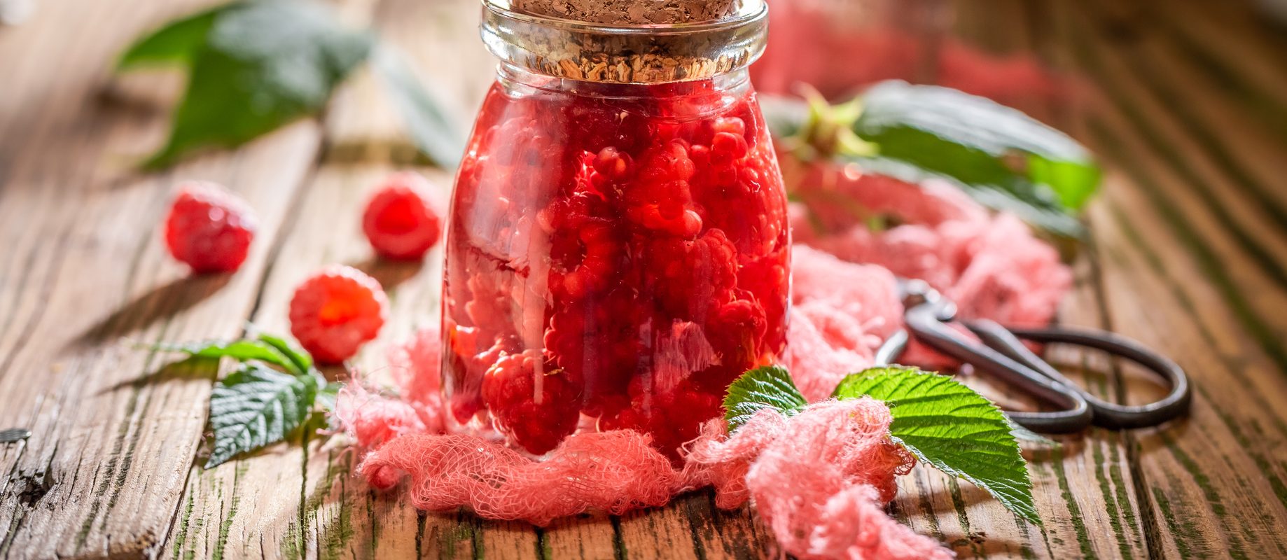 Nalewka z malin - jak ją zrobić? Przepis na malinówkę. Nalewka malinowa w słoiku na drewnianym blacie.