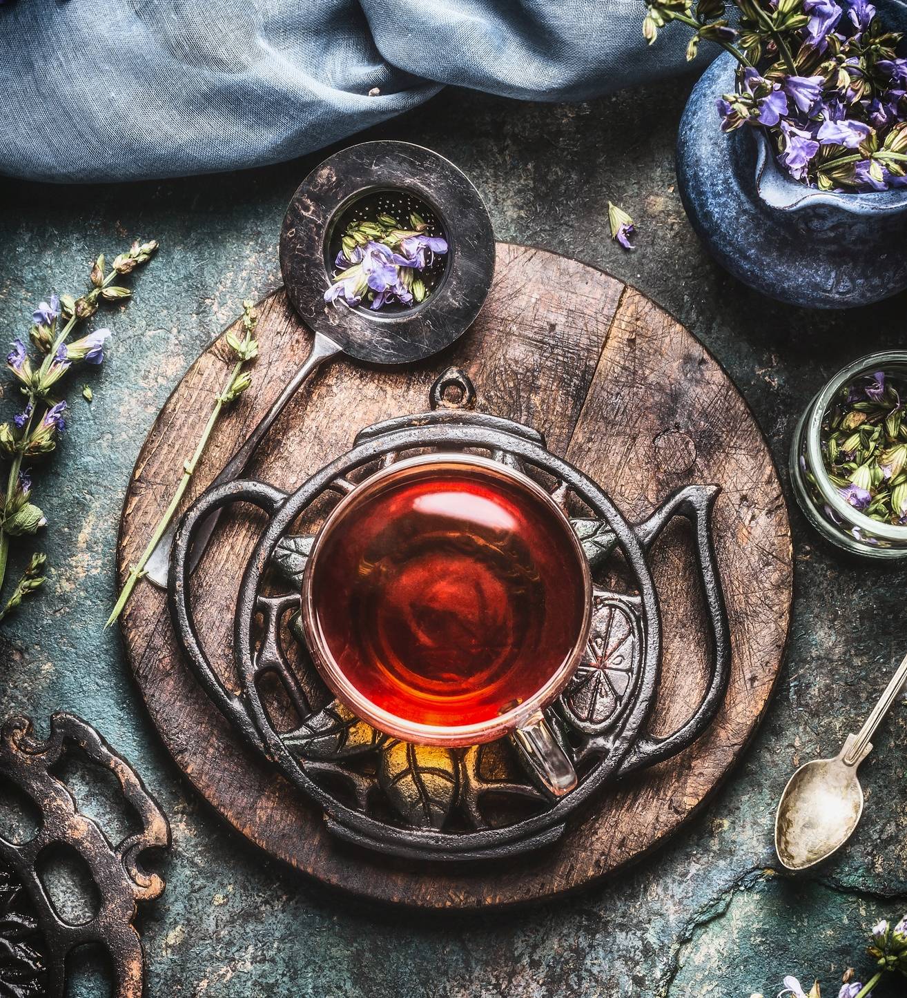 Zioła na cukrzycę typu 2. Filiżanka naparu stoi na drewnianej tacce, obok leżą suszone zioła i niebieskie kwiatki.