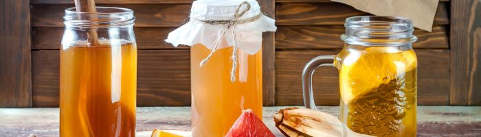 Napój kombucha - naturalny probiotyk z grzybka kombuchy (grzybka herbacianego. Herbata kombucha w słoikach na blacie, obok leżą kawałki cytrusów.