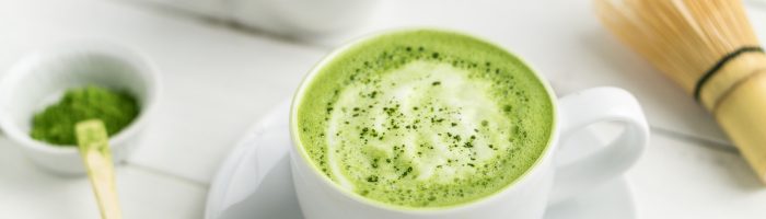 Zielona herbata matcha. Napój z zieloną herbatą matcha (matcha latte) w białej filiżance, obok leżą akcesoria do parzenia sproszkowanej zielonej herbaty..