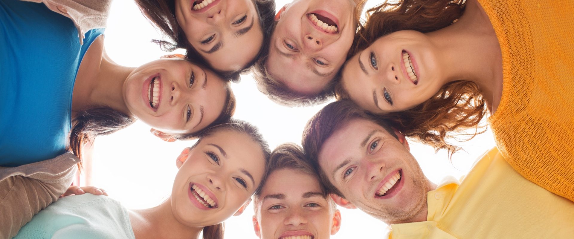 Homeopatia, leki homeopatyczne dla dzieci i dla nastolatków. Grupa uśmiechniętych nastolatków pochyla się w kręgu i patrzy w dół do obiektywu.