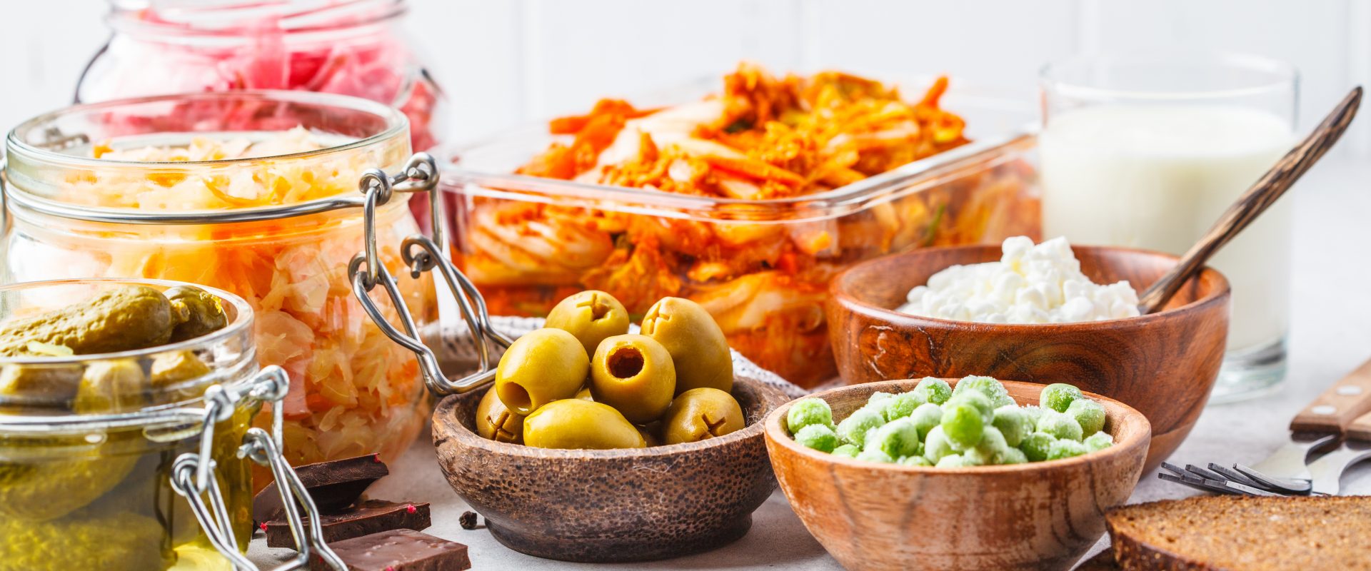 Naturalne probiotyki - czy mogą zastąpić suplementy probiotyczne? Fermentowana żywność w miseczkach i słoikach na białym kuchennym blacie.