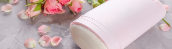 Jak wybrać bezpieczny naturalny dezodorant i antyperspirant? Dezodorant w różowym opakowaniu, wokół leżą róże.
