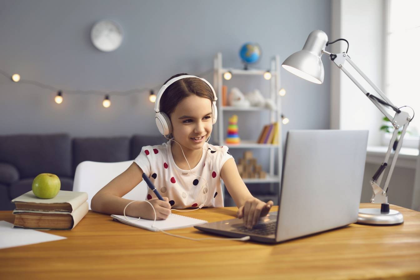 Czy nauka zdalne przyniosła dzieciom jakieś korzyści? Dziewczynka ze słuchawkami na uszach siedzi w swoim pokoju przed laptopem i uczestniczy w lekcjach online.