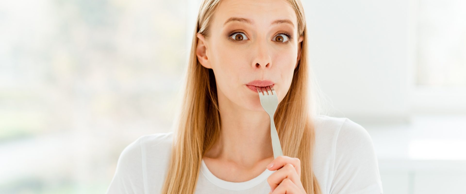 Niesmak w ustach - co może oznaczać metaliczny posmak w ustach? Młoda kobieta oblizuje widelec.