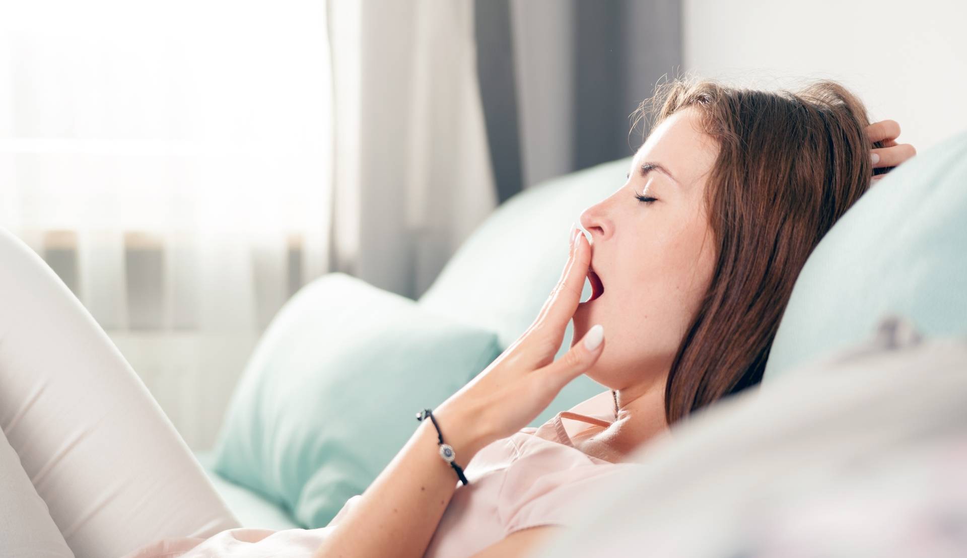 Grzybica układu pokarmowego - objawy kandydozy. Młoda kobieta ziewa na kanapie.