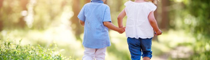 Borelioza u dzieci - jak ochronić dziecko przed kleszczami i jak wyciągnąć kleszcza? Dziewczynka i chłopiec idą za rękę przez las.