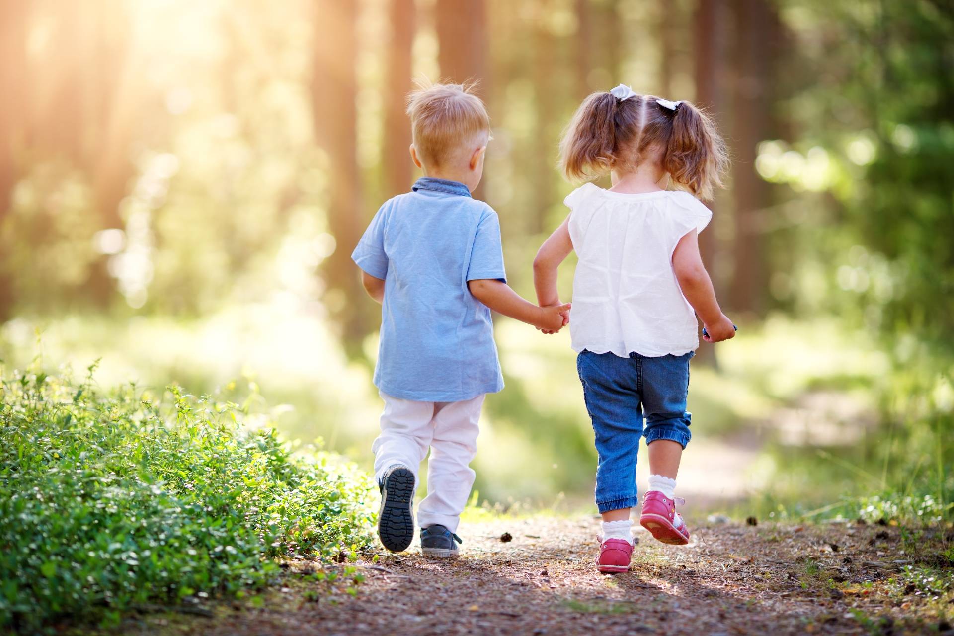 Borelioza u dzieci - jak ochronić dziecko przed kleszczami i jak wyciągnąć kleszcza? Dziewczynka i chłopiec idą za rękę przez las.