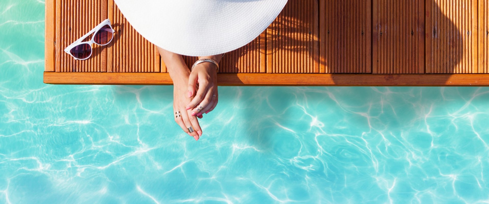 Jak się bezpiecznie opalać przy problemach z cerą? Kobieta wypoczywa w basenie, chroniąc się przed słońcem wielkim kapeluszem.