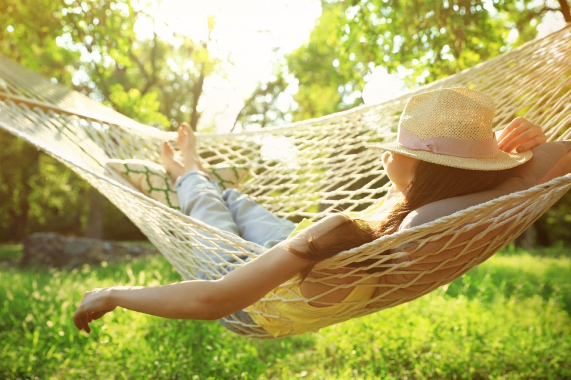 Na czym polega odpoczynek? Jak nauczyć się relaksować? O sztuce odpoczywania pisze Beata Sadowska, dziennikarka. Kobieta odpoczywa w hamaku w letni dzień, zakrywając twarz słomkowym kapeluszem.