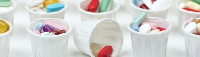 Antybiotyki - czemu przestają działać? Czym jest antybiotykooporność? Czy grozi nam epidemia superbakterii? Kolorowe pastylki w białych plastikowych kubeczkach medycznych, jeden z nich jest przewrócony i wysypały się z niego leki.