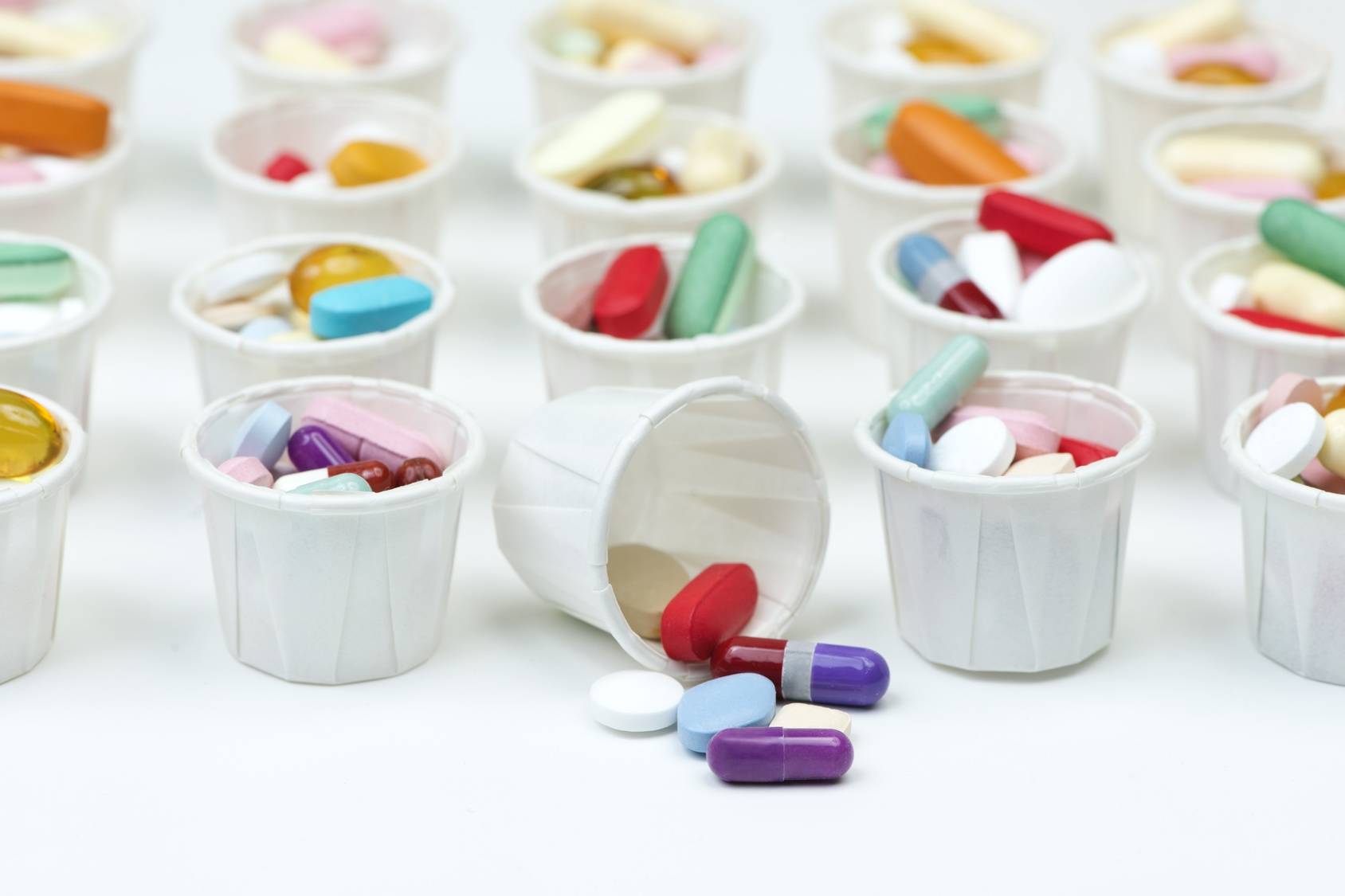 Antybiotyki - czemu przestają działać? Czym jest antybiotykooporność? Czy grozi nam epidemia superbakterii? Kolorowe pastylki w białych plastikowych kubeczkach medycznych, jeden z nich jest przewrócony i wysypały się z niego leki.