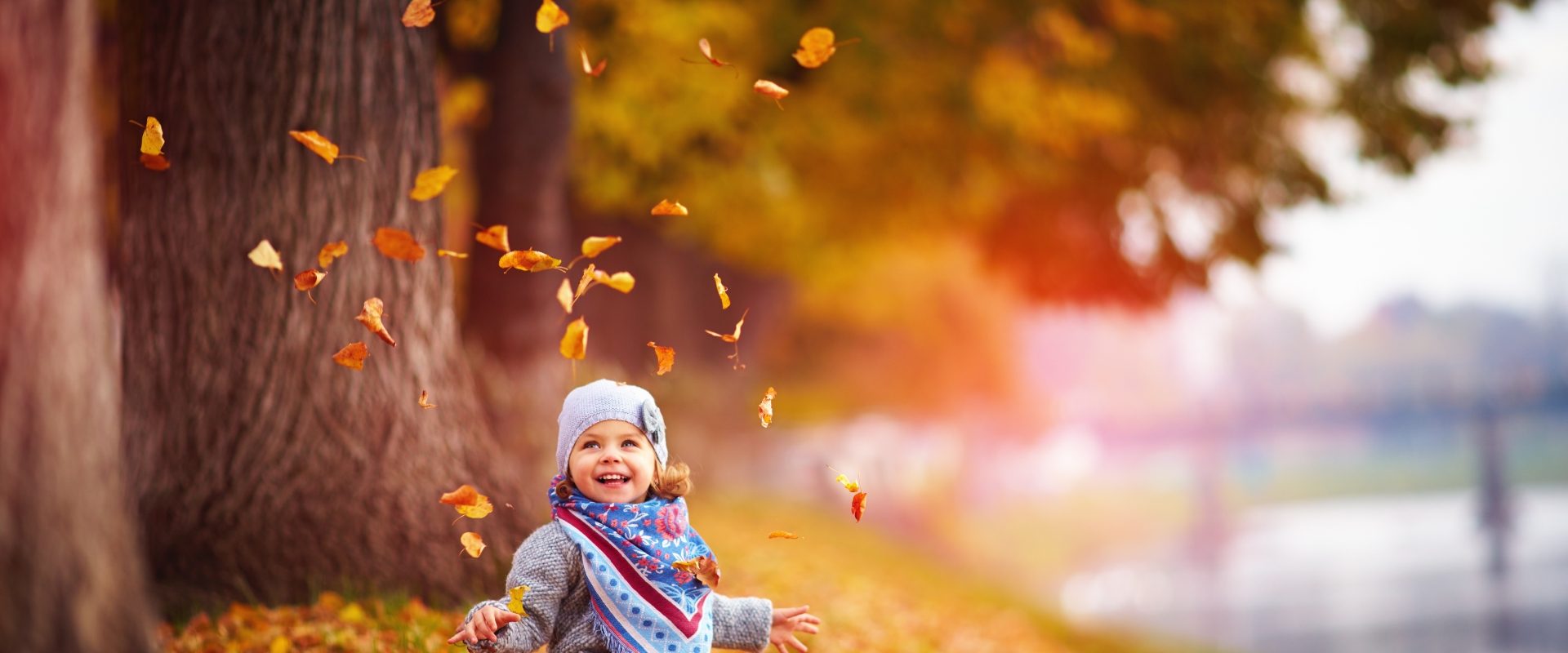 Jak wzmocnić odporność u dzieci? Mała dziewczynka bawi się jesiennymi liśćmi.
