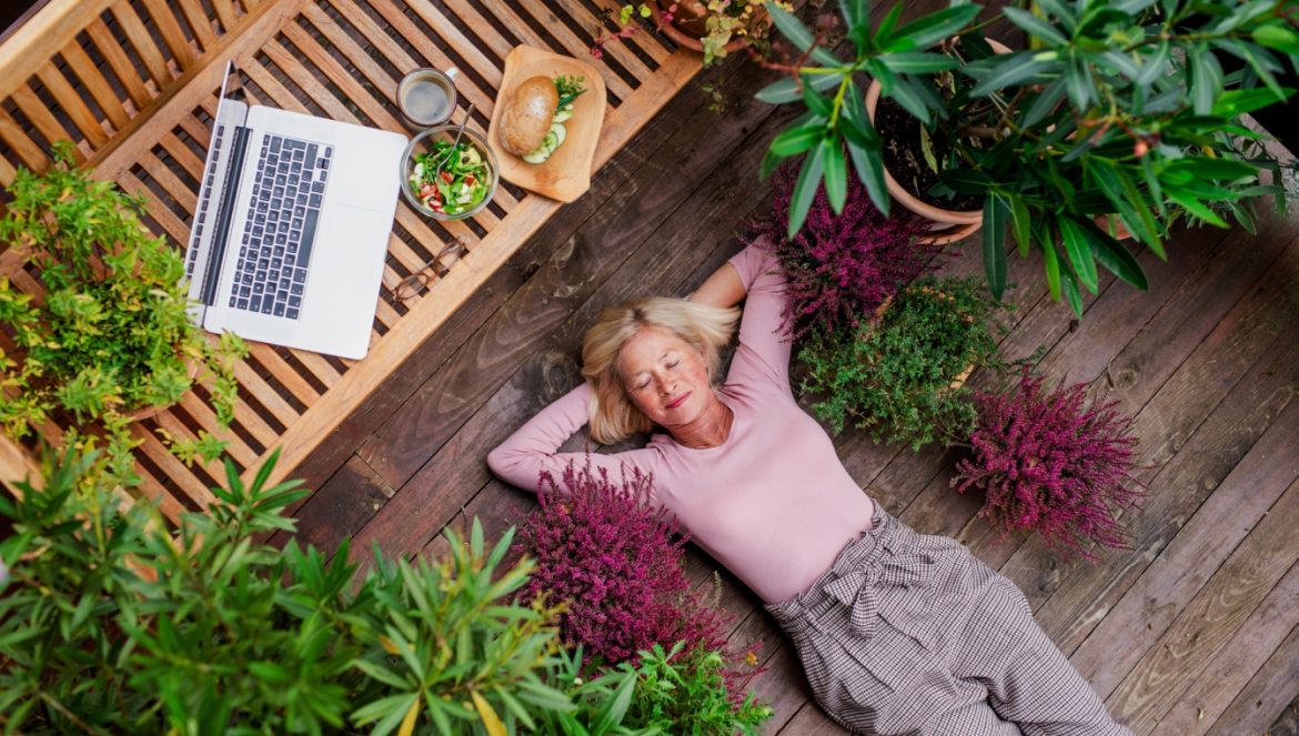 Jak zrobić ogródek na balkonie? Kobieta seniorka wypoczywa na zielonym balkonie.