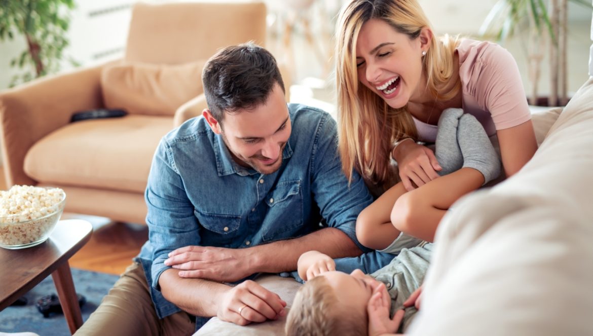 Oksytocyna - hormon miłości i przywiązania. Szczęśliwa rodzina w domu, rodzice bawią się ze swoim synkiem w salonie.
