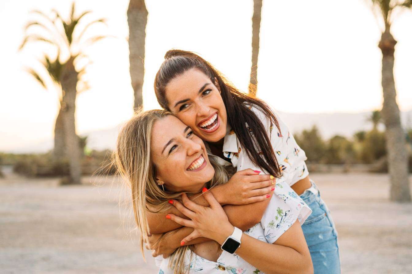 Czym jest oksytocyna, zwana hormonem miłości i przywiązania? Dwie uśmiechnięte przyjaciółki przytulają się do siebie, spędzając wspólnie czas latem na plaży.