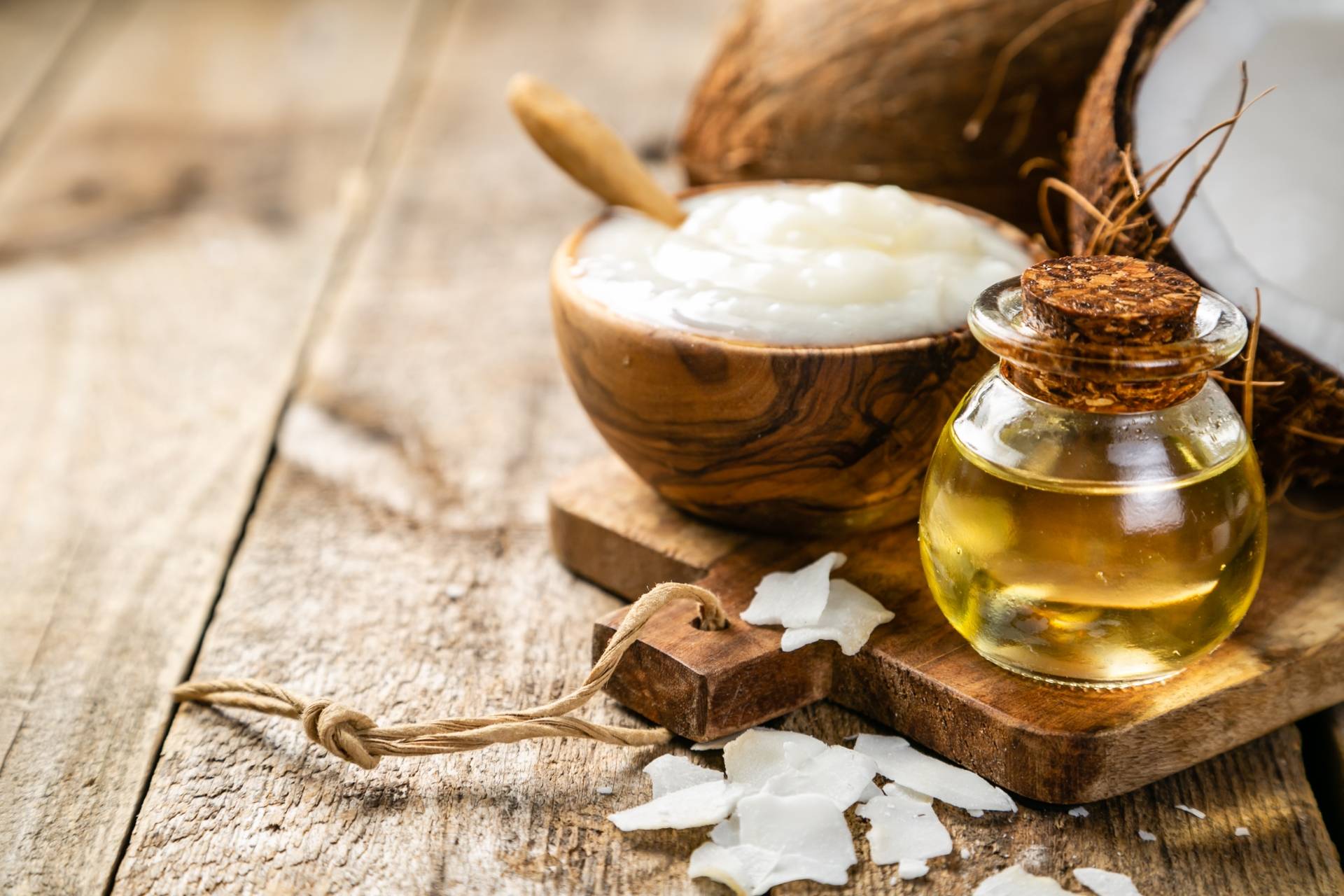Olej kokosowy w miseczce i olej w butelce na drewnianym blacie.
