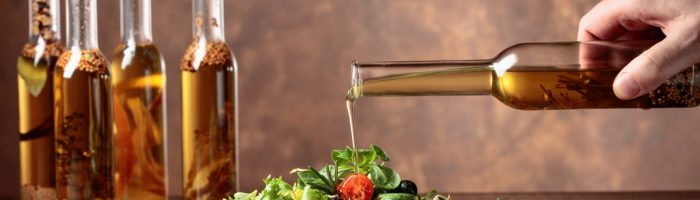 Zdrowe tłuszcze do spożywania na zimno. Zielona sałatka z pomidorami polewana oliwą z oliwek z butelki.