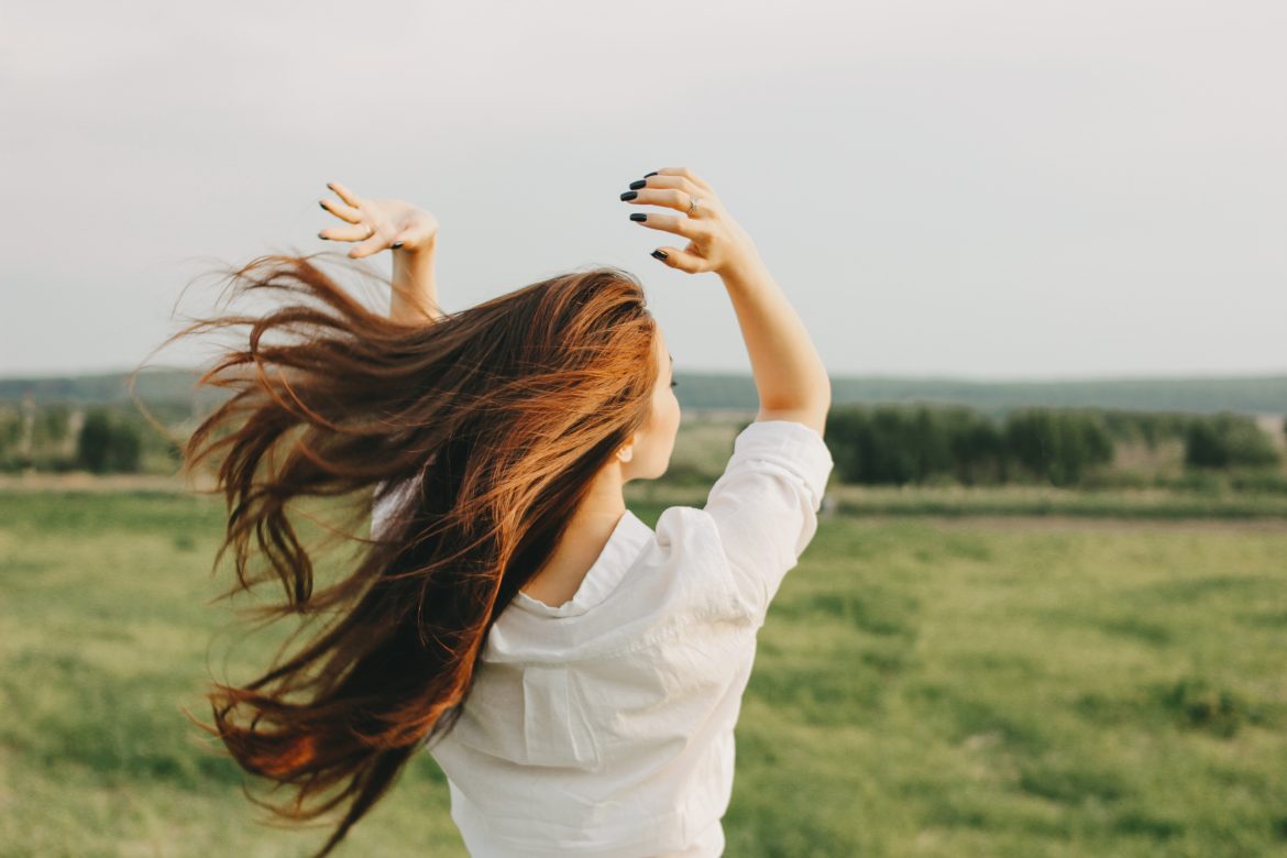 Mycie włosów metodą OMO - na czym polega? Dziewczyna z rozwianymi przez wiatr rudymi włosami stoi na łące.
