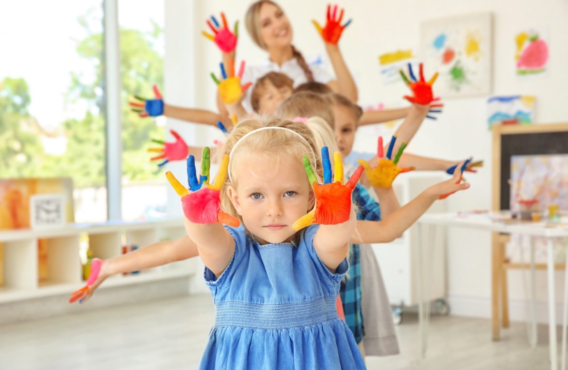 Owsiki u dzieci. Przedszkolaki i przedszkolanka pozują do zdjęcia z dłońmi pomalowanymi farbą.