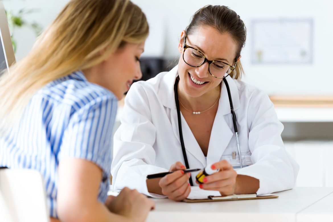 Zespół policystycznych jajników (PCOS) – objawy, przyczyny, badania, leczenie. Młoda kobieta na wizycie u ginekologa słucha zaleceń lekarki.