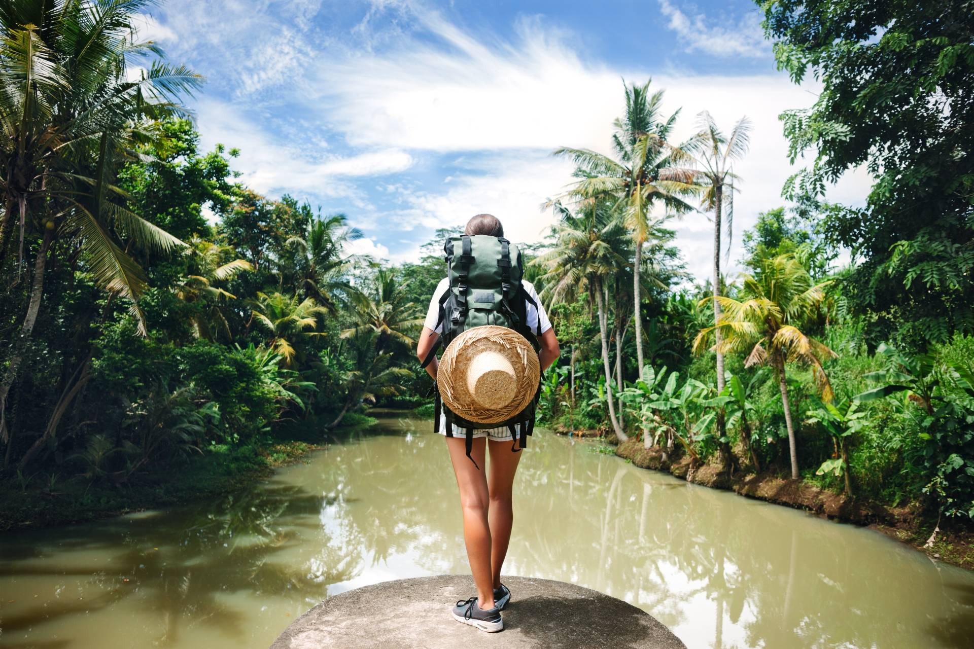 Apteczka podróżnika - jakie leki homeopatyczne pierwszej pomocy zabrać na wakacje? Podróżniczka z plecakiem stoi na tle dżungli w tropikach.